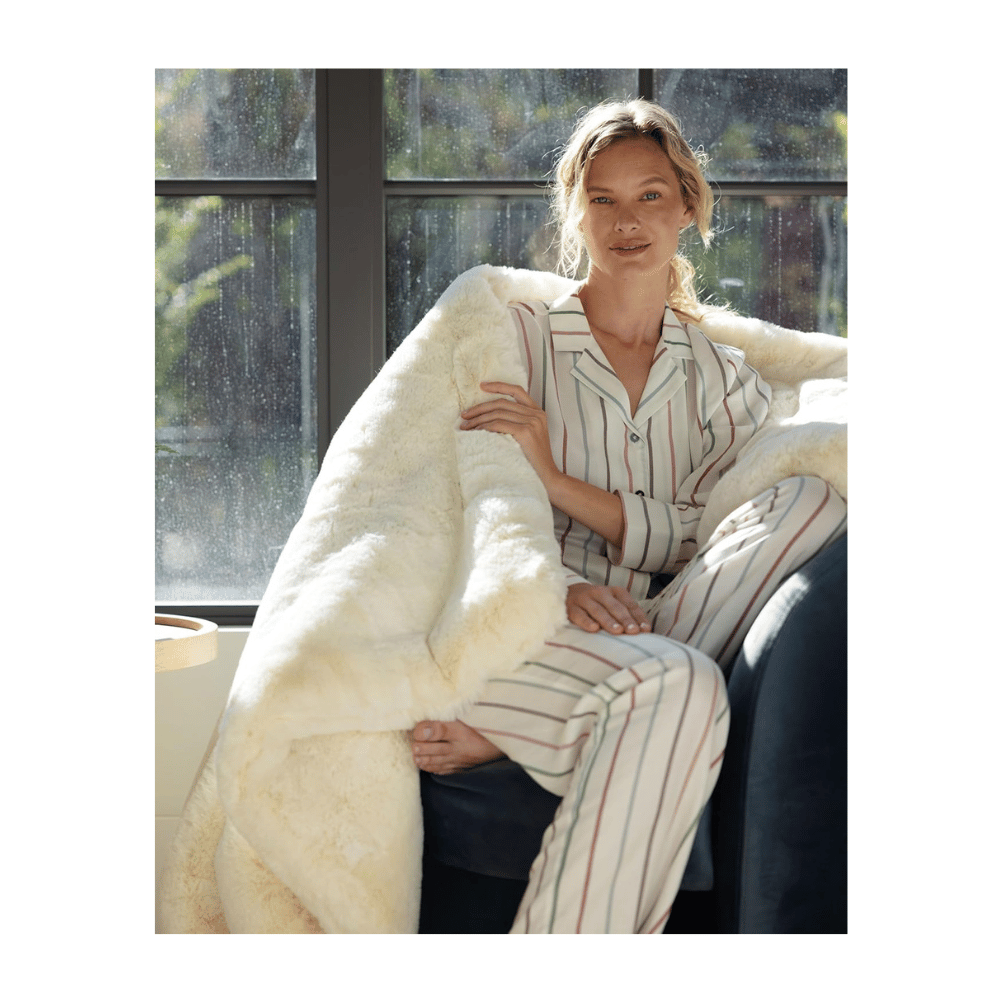 Woman sitting by window wrapped in Cozy Earth Cuddle Blanket, ivory bamboo throw for year-round relaxation.