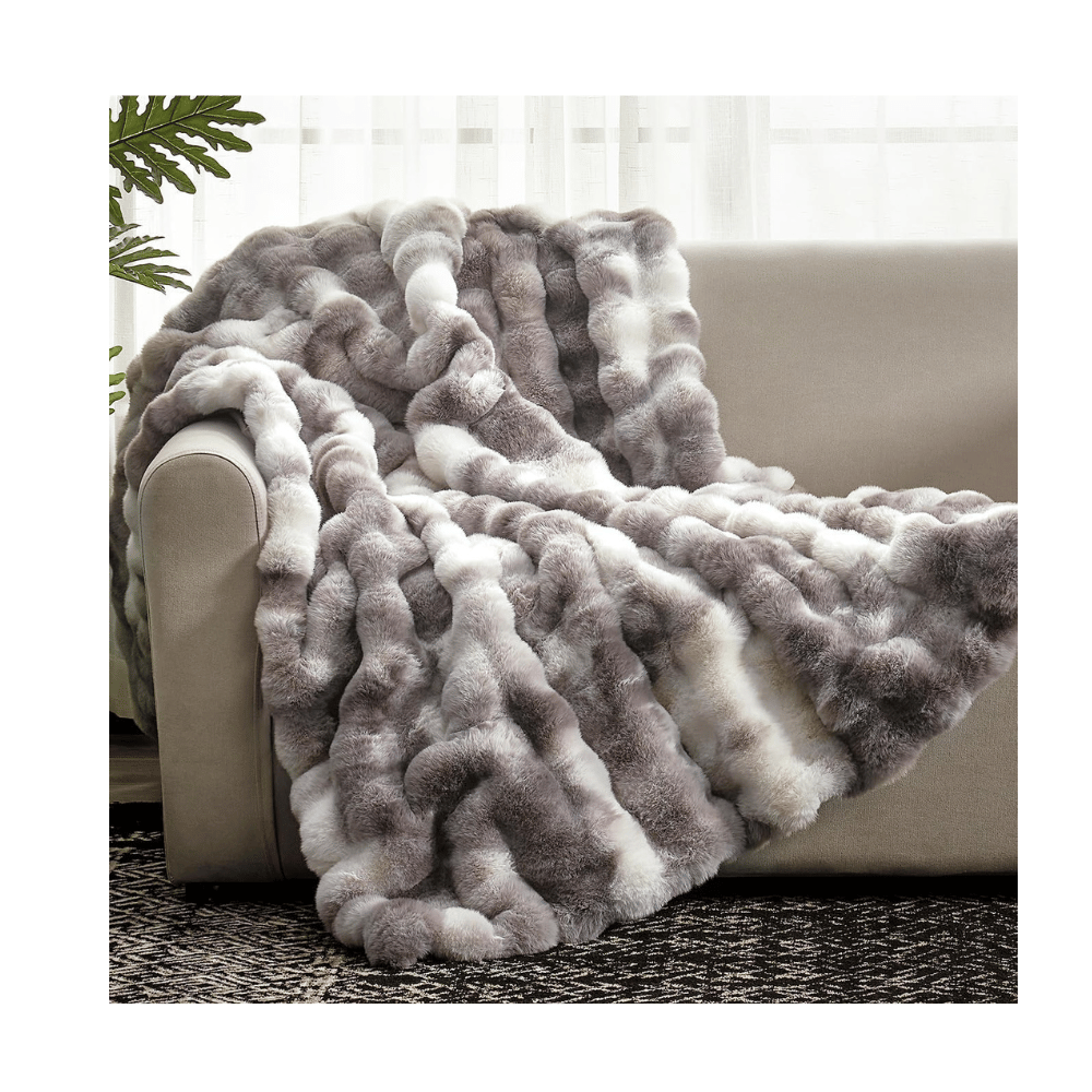 Gray and white Cozy Bliss Faux Fur Blanket draped over sofa, featuring soft gradient pattern and fluffy faux fur.