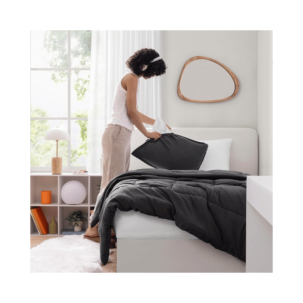 Woman arranging pillows on bed with UGG Down Alternative Comforter (Credit: UGG / Amazon)
