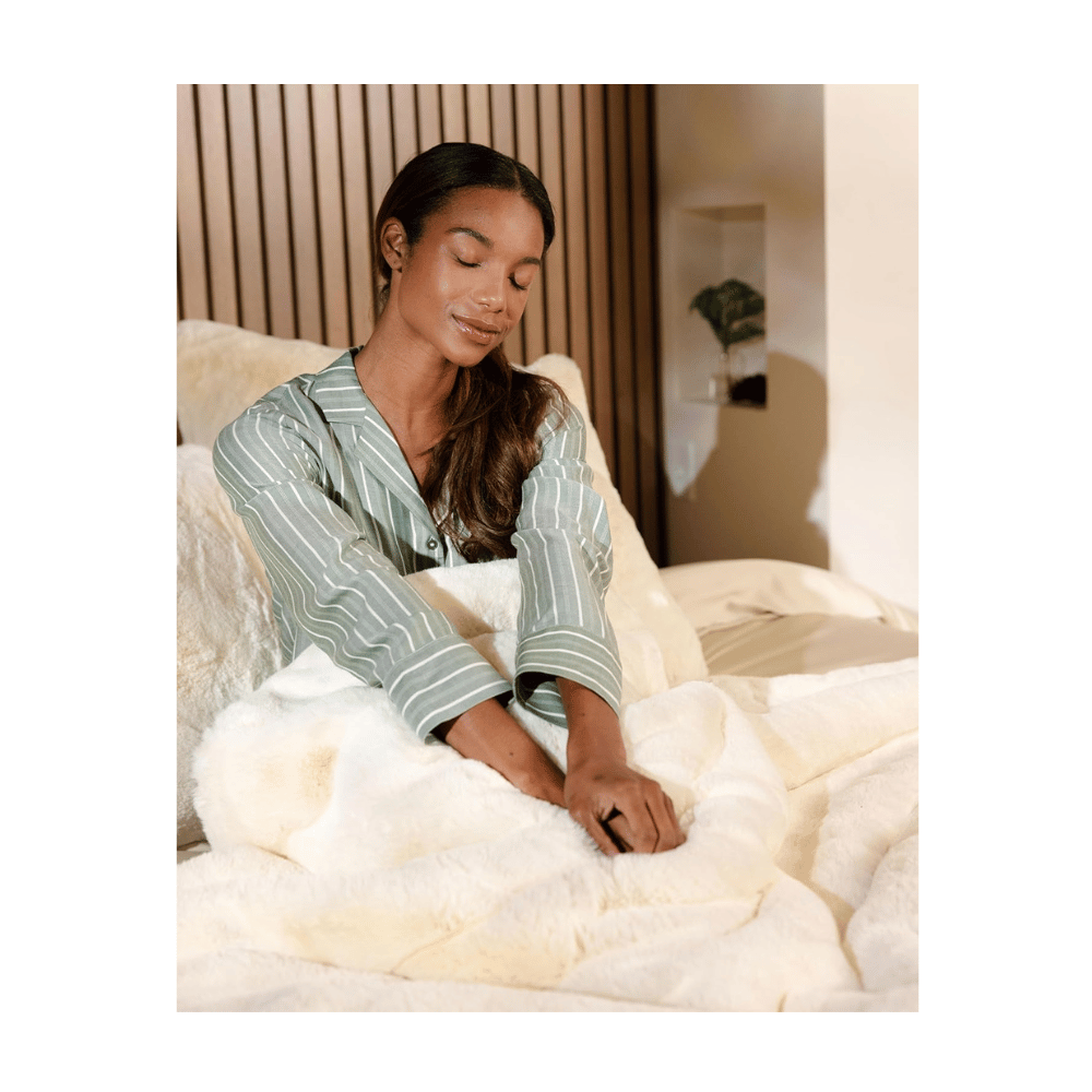Woman relaxing in bed wrapped in Cozy Earth Cuddle Blanket, soft bamboo viscose throw offering luxury comfort.