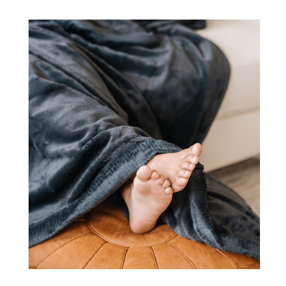 Person wrapped in gray Saranoni Oversized Luxury Blanket on couch, showing lush plush texture and cozy warmth.
