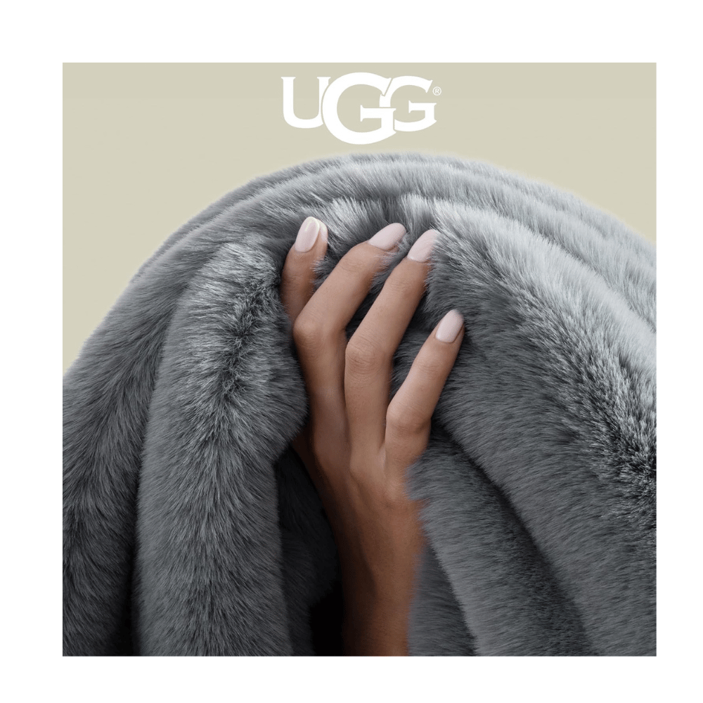 Hand holding gray UGG Plush Faux Fur Blanket highlighting ultra-soft faux fur texture and luxurious finish.